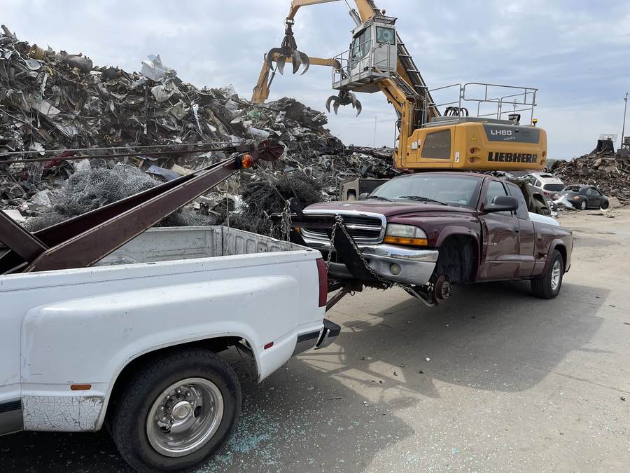 MankStar tow truck carrying a vehicle at a salvage yard.